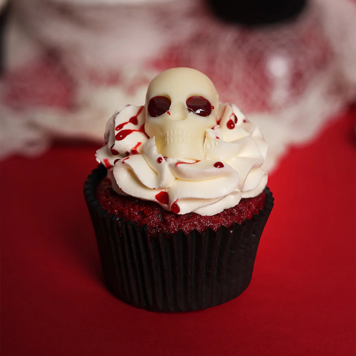 Halloween Themed Red Velvet Cupcake decorated with white chocolate skull and blood syrup.